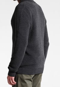 Mörkgrå tröja med en texturerad ribbad design, åtsittande ärmslut och rundad halsringning, tillverkad av stickad tyg.