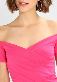 Top ajustado sin hombros en una mezcla de algodón de color rosa brillante, con mangas cortas y un diseño cruzado en el escote y el busto.