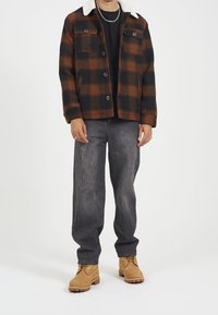 Randig jacka i mörk orange och svart med två bröstfickor. Kombinerad med gråa vida jeans och bruna snörskor.