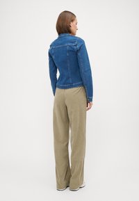 Denim jakna u plavoj boji s dugim rukavima, prilagođenim krojem i klasičnim ovratnikom. Uparen s širokim svijetlosmešanim hlačama i bijelim cipelama.