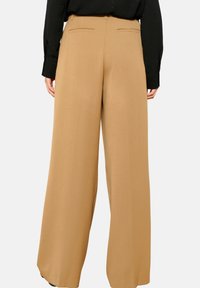 Wijdvallende broeken van een lichte tan stof, met een gladde textuur, een aansluitende taille en twee achterzakken. GStyled met een zwart top.