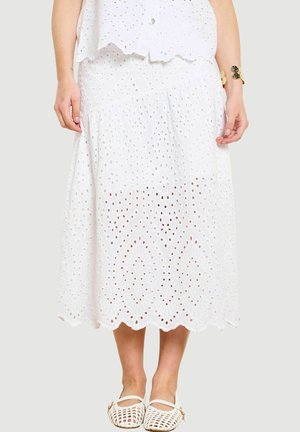 Valge silmaauguline midi seelik silutud äärega, kantud sobiva topi ja valgete punutud Mary Jane jalanõudega, vasakul randmel kuldne käevõru.