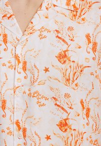 Camisa de manga corta en tejido ligero con un patrón de vida marina en color naranja sobre un fondo blanco, con cierre de botones en la parte delantera y cuello clásico.