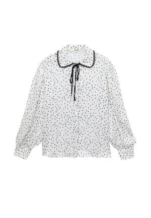 Blusa blanca con lunares negros, con cuello redondeado, ribete negro y cierre de lazo, mangas largas abullonadas y parte delantera con botones.