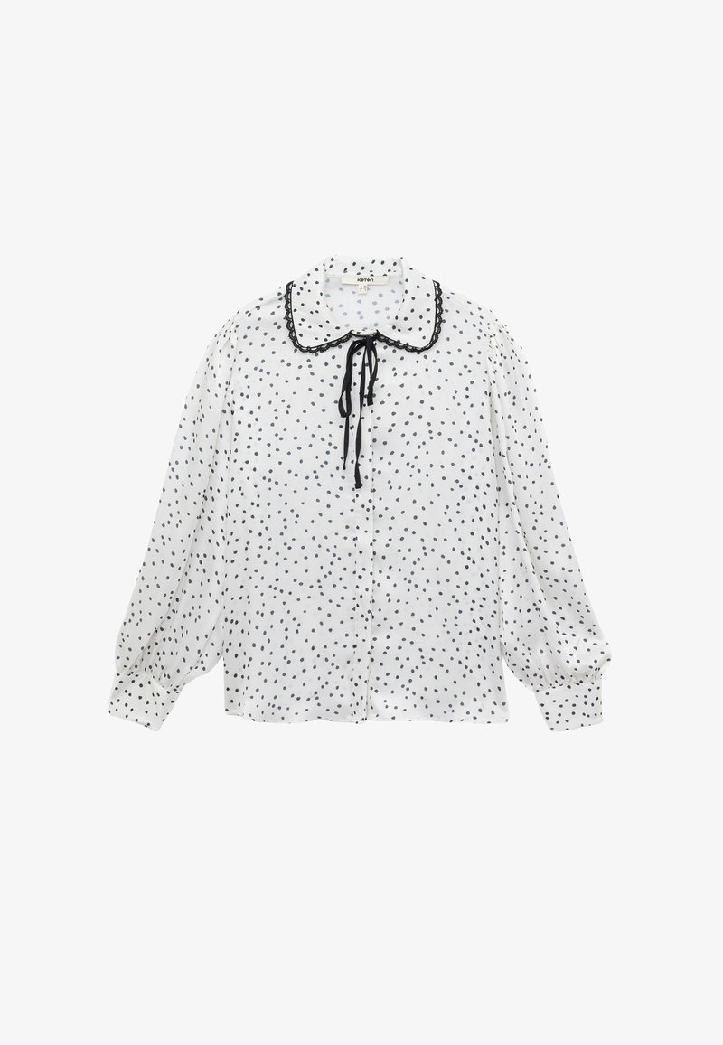 Hvid bluse med sorte prikker, der har en rund krave, sort kant, og en bindelukning, med lange pufærmer og knaplukning foran.