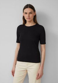 Schwarzes, geripptes Kurzarmshirt mit Rundhalsausschnitt, tailliertem Design und glatter Textur. Kombiniert mit hellen Hosen.