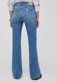 Jean en denim bleu évasé avec cinq poches, coutures visibles et une étiquette en cuir à la taille. Texture lisse avec un effet délavé clair.