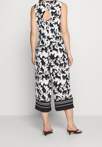 Jumpsuit floral en blanco y negro con diseño sin mangas, espalda con abertura en forma de clave, patas anchas y cortas, y acentos a rayas en los puños.
