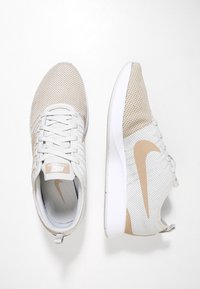Lätta träningsskor med ett vitt och beige nätöverdrag, snörning och en vit sula. Utrustad med Nike swoosh-logotyp i beige på sidan.