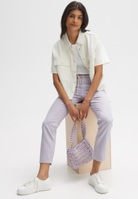 Giacca di jeans bianca cropped, t-shirt grigia, pantaloni lilla chiaro, sneakers bianche e una piccola borsa intessuta lilla. Design minimalista, look casual.