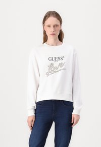 Felpa bianca in cotone con logo "GUESS" e decorazione in argento "Love" sulla parte anteriore, caratterizzata da maniche lunghe e un design corto.