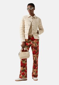 Béžová prošívaná bunda se stříbrnými knoflíky, tělové tričko, květinové kalhoty v červené a zelené barvě, krémová kabelka a bílé tenisky. Celkový vzhled doplňují kulaté sluneční brýle.