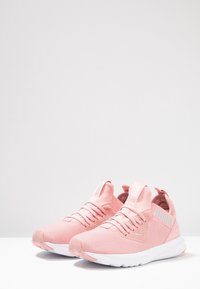 Un paio di scarpe da corsa Puma rosa chiaro con suole bianche, tomaia in rete e lacci, mostrato su uno sfondo bianco semplice.