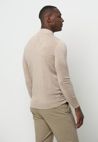 Beige pullover trui met een hoge kraag, lange mouwen en een gladde textuur, gecombineerd met lichtgekleurde broeken.