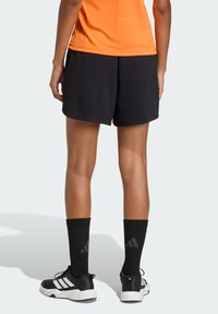 Pantalones cortos deportivos negros con una tela texturizada, una cinturilla elástica, combinados con calcetines negros y zapatillas deportivas negras con detalles en blanco.