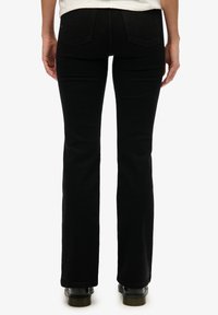 Zwarte flared jeans met een gladde textuur, standaard achterzakken en een taille met middenhoogte, gecombineerd met zwarte schoenen.