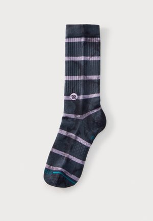 Chaussette noire mi-mollet avec des rayures horizontales violet clair, un petit logo circulaire près de la cheville et un texte turquoise sur l'orteil.