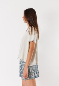 Top grigio chiaro, leggero e con maniche corte, con scollatura a V; abbinato a pantaloni corti blu con un motivo a foglie. Tessuto morbido in misto cotone.