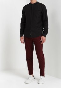 Svart långärmad skjorta med mandarin-krage, knäppt fram och en bröstficka; matchat med vinröda slim fit byxor och vita sneakers.