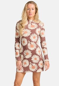 Robe à manches longues marron avec un grand motif de marguerite en crème et pêche. Texture côtelée, design ajusté et longueur mini.