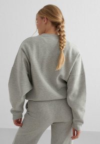 Gray cropped sweatshirt with loose-fitting sleeves, made of soft fabric, paired with matching gray pants. Features a simple, smooth texture.