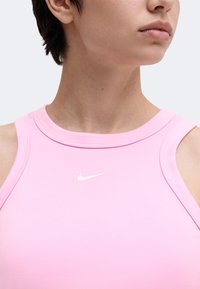 Gros plan d'une personne portant un haut rose sans manches avec un petit logo Nike blanc sur la poitrine, la tête légèrement tournée de côté.