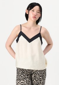 Camiseta crema con un acento en forma de V negro, con tirantes finos. Combinada con pantalones estampados en rayas de cebra en negro y beige.