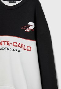 Zwart-witte sweatshirt met rood geborduurde tekst "MONTE-CARLO" en "CÔTE D'AZUR," met het nummer "7" en een handtekeningdetail.