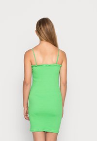 Zielona, żeberkowana sukienka bodycon z cienkimi ramiączkami i falbaną przy dekolcie. Materiał jest gładki i dopasowany, podkreślający smukłą sylwetkę.