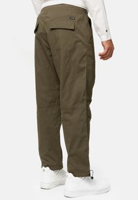 Khaki cargo bukser med en afslappet pasform, der har en baglomme, sidelommer og elastiske manchetter, parret med hvide sneakers.