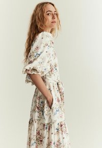 Blomstret kjole i blød, let stof; har flæseærmer, et bindebælte og en lagdelt nederdel. Farverne inkluderer creme, pink og blå.