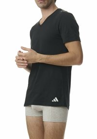 Svart bomulls T-shirt med V-ringning och korta ärmar; har en vit Adidas-logga på nedre vänstra sidan. Grå kalsonger synliga under.