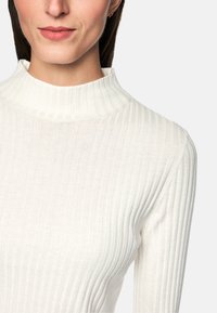 Gestreifter Rollkragenpullover in Off-White, mit körpernahem Schnitt und strukturiertem Stoff. Nahaufnahme betont die Details von Hals und Schultern.