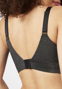 Reggiseno nero con una texture scintillante, dotato di spalline regolabili e una banda ampia. Design a forma di V sul retro con chiusura a gancio e occhiello.