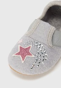 Sapatilha cinza com fita elástica, apresentando uma estrela em glitter rosa e acentos de lantejoulas prateadas; bico arredondado e forro interior suave.