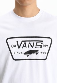 Weißes Baumwoll-T-Shirt mit einem schwarzen Grafikdruck, der "CA Vans NY" und einer Skateboard-Illustration zeigt. Rundum gerippter Halsausschnitt, kurze Ärmel.