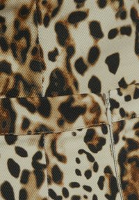 Tissu en imprimé léopard avec un fond beige et des taches brunes et noires, montrant un tissage texturé et un détail de fermeture éclair dissimulé.