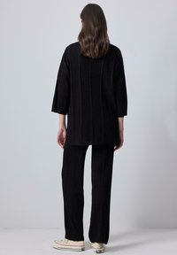 Black ribbed knit top with 3/4 sleeves and matching ribbed pants, both featuring a relaxed fit and textured fabric. Worn with white sneakers.