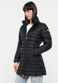 Zwarte pufferjack met een verticale quiltontwerp, hoge kraag en ritsluiting. Beschikt over een oranje ritslip en logoaccent.
