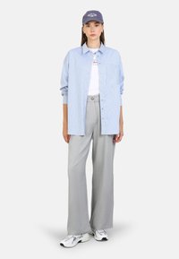 Blau-weiß gestreiftes Hemd mit Knopfschluss, graue weit geschnittene Hose und eine dunkelblaue Mütze. Verfügt über eine Brusttasche und lässige Sneaker.