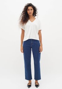 Vit V-ringad kortärmad topp kombinerad med högmidjade, raka blå jeans och svarta spetsiga flats.