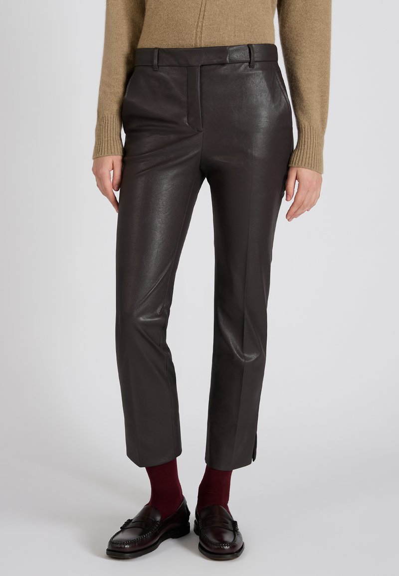 Brązowe skórzane spodnie o świecącej powierzchni, dopasowane w talii, z bocznymi kieszeniami i długości do kostek, w zestawieniu z bordowymi skarpetkami i mokasynami.