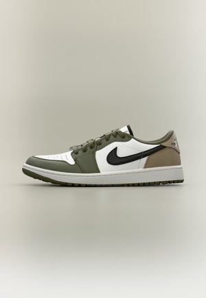 Une sneaker Nike basse avec un Swoosh noir, des empiècements blancs, des superpositions et des lacets vert olive, ainsi qu’un talon beige, vue de profil.
