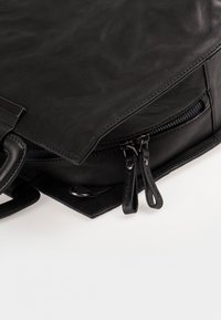 Musta nahkalaukku, jossa on teksturoitu pinta, kaksi vetoketjua, jämäkkä muotoilu, tukevat kahvat ja metallinen yksityiskohta.