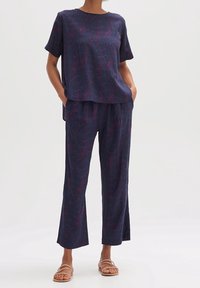 Donkerblauw, kortärmelig shirt met verticale lijnen in roze en paars, gecombineerd met bijpassende losse broek. Beide hebben een ontspannen pasvorm en een gladde textuur.