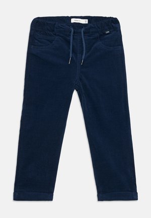 Pantalon bleu marine en tissu doux avec une taille élastique, un cordon de serrage, deux poches avant et des ourlets retroussés. Étiquette de la marque visible sur la ceinture.