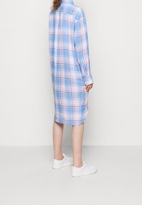 Lång rutig skjortklänning i ljusblått, rosa och vitt. Har en knapp-up krage, lång ärm och sidoföre. Bärs med vita sneakers.