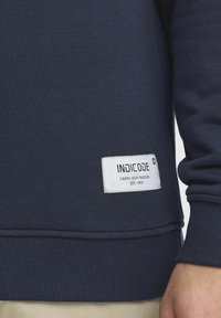 Navy sweatshirt with ribbed cuffs and hem. Features a white label reading "INDICODE" with the text "CARRY OUR PASSION" in black.