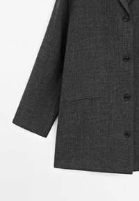 Blazer en laine gris foncé avec manches longues, trois boutons noirs visibles et une poche passepoilée horizontale en bas à l'avant.