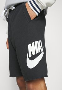 Shorts en coton noir avec une ceinture élastique, des poches latérales et un grand logo Nike blanc sur la cuisse gauche, avec un ourlet effiloché.